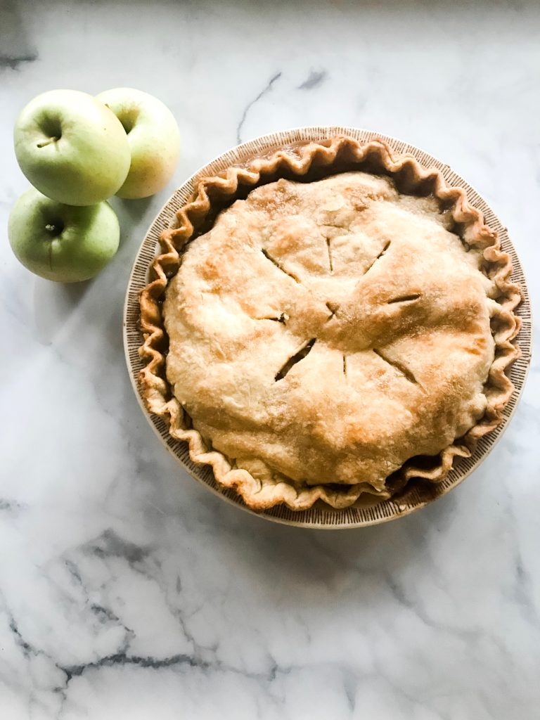 Fresh baked apple pie next to a stack of green apples