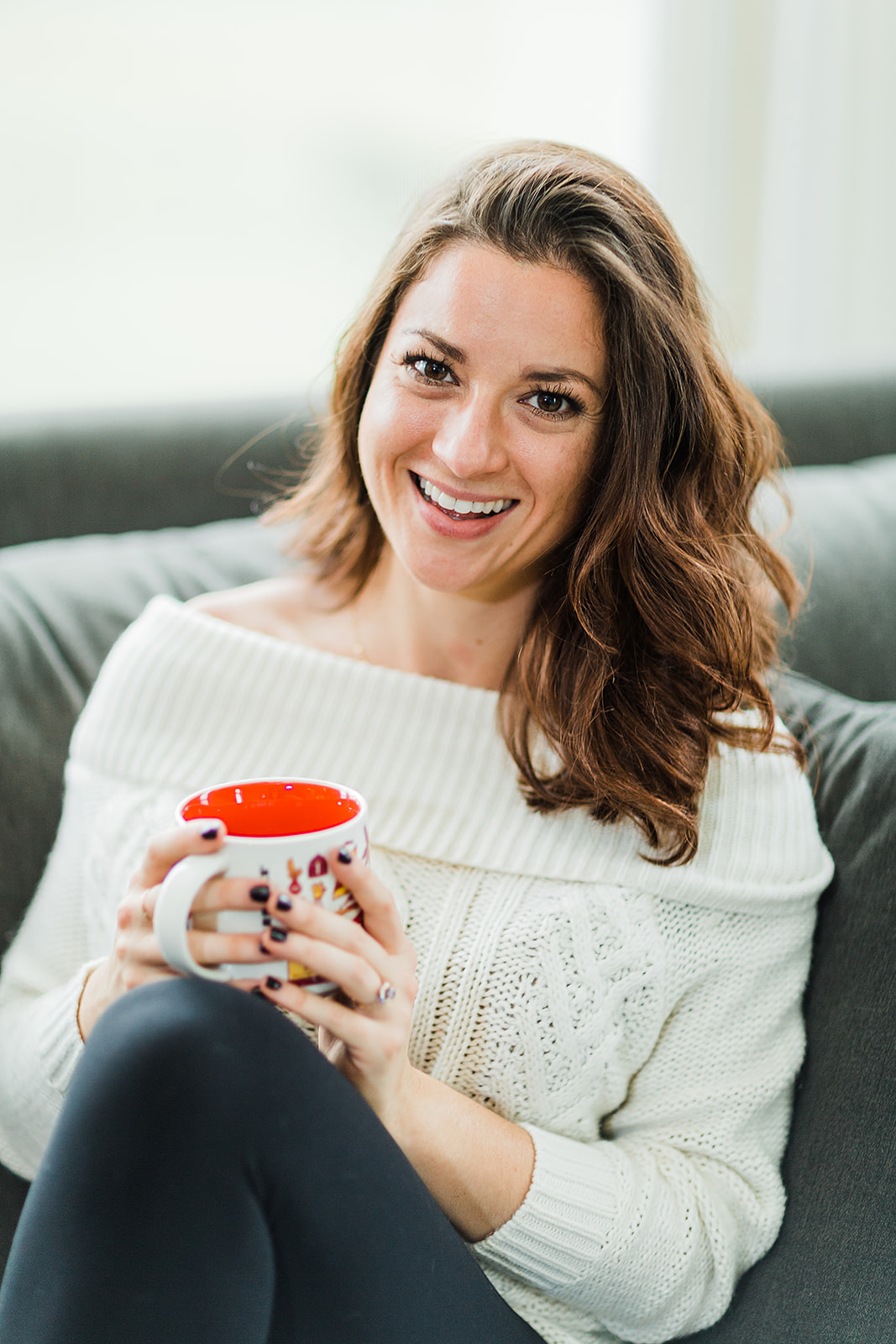 Jen Lyman holds a mug, wearing a cozy sweater