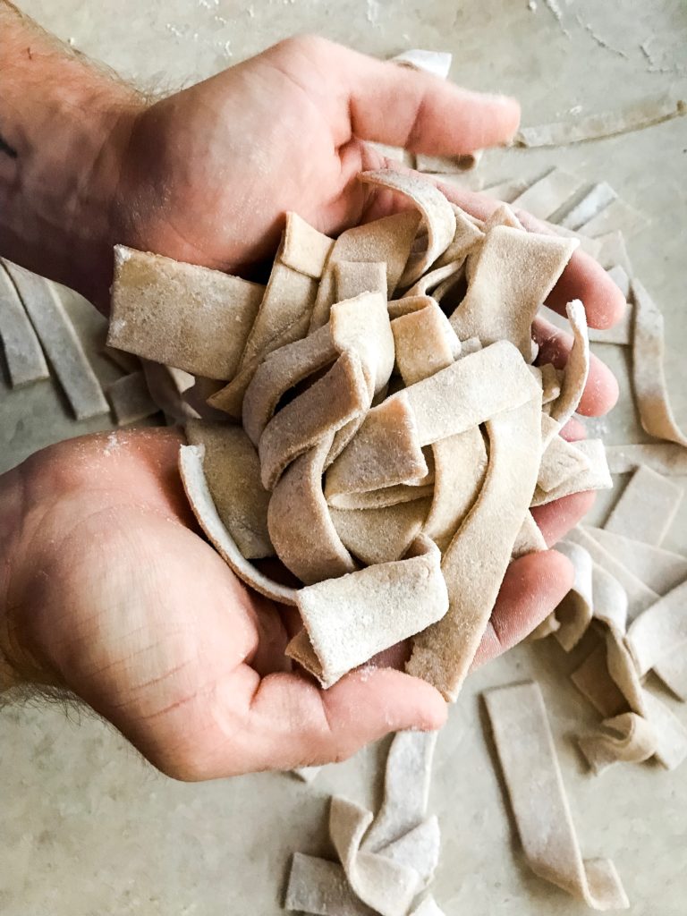 Freshly prepared and cut egg noodles being held to show shape and texture