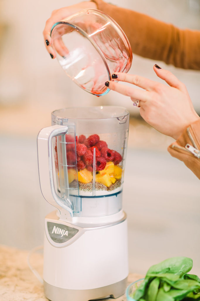 Jen Lyman pours frozen raspberries into blender with mango and flax seed to make a smoothie