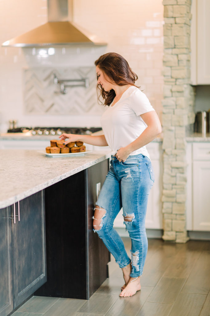 Jen Lyman stands in a well-lit kitchen reaching for a muffin