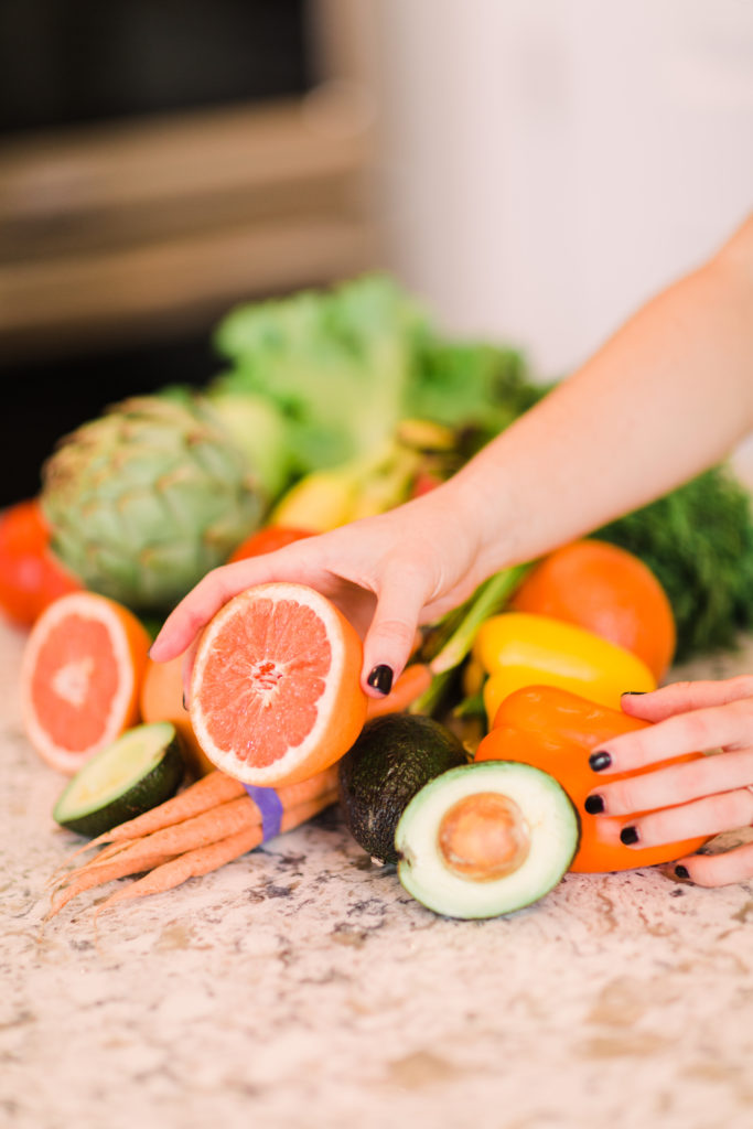 Hand placing grapefruit into a pile of fruits and vegetables