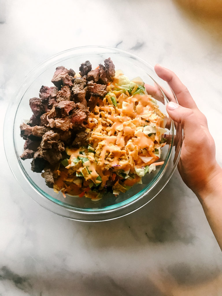 New Leaf Nutrition's dietitian Jen Lyman's hand holding a bowl of salad topped with steak