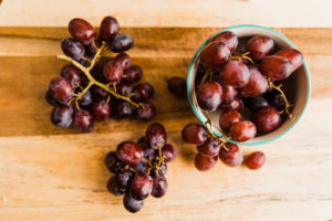 Three clusters of purple grapes on a wooden cutting board