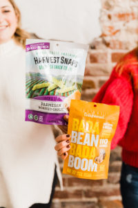 Bag of crunchy roasted peas and a bag of bada bean bada boom beans are held by dietitians Alex Harris and Jen Lyman