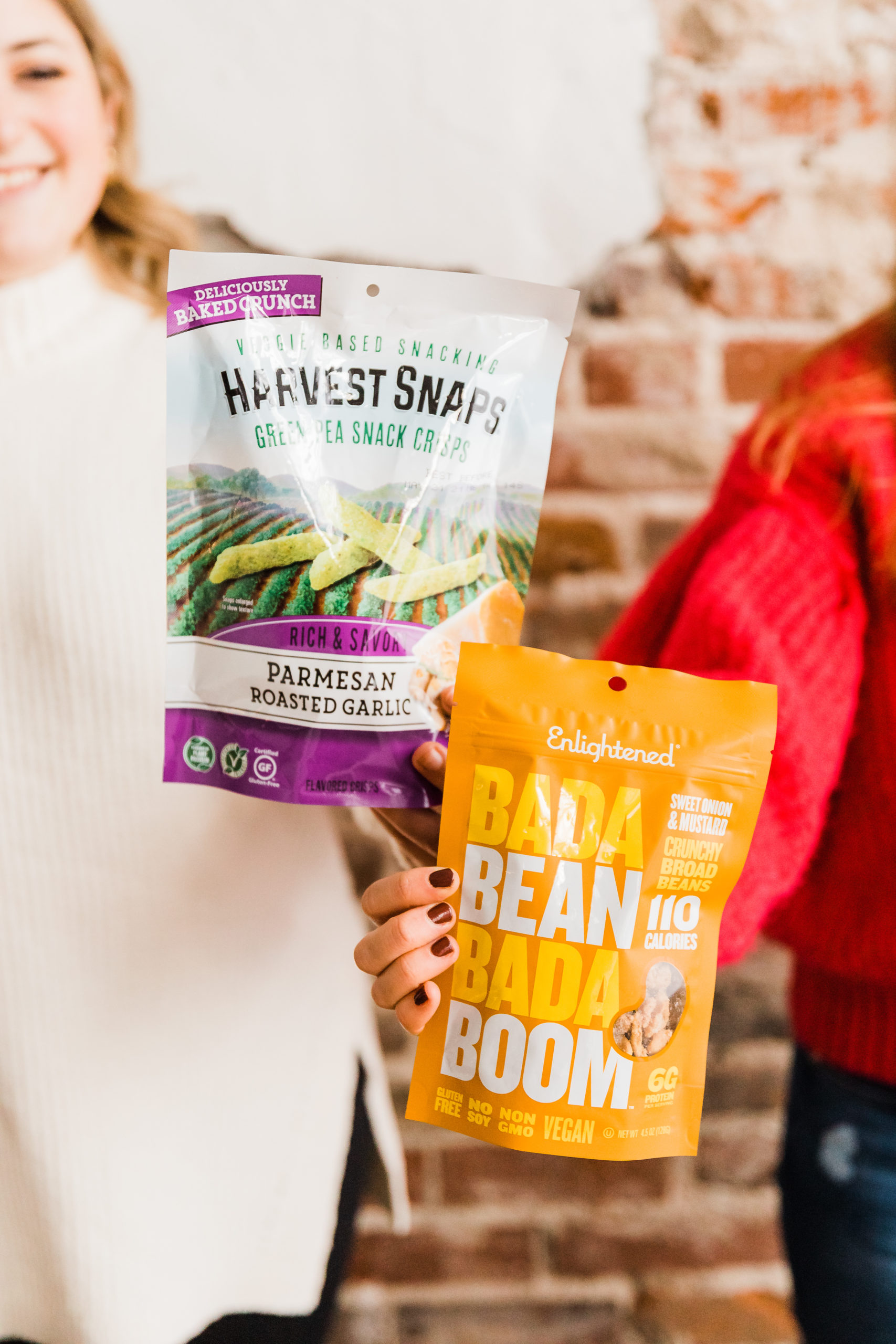 Bag of crunchy roasted peas and a bag of bada bean bada boom beans are held by dietitians Alex Harris and Jen Lyman